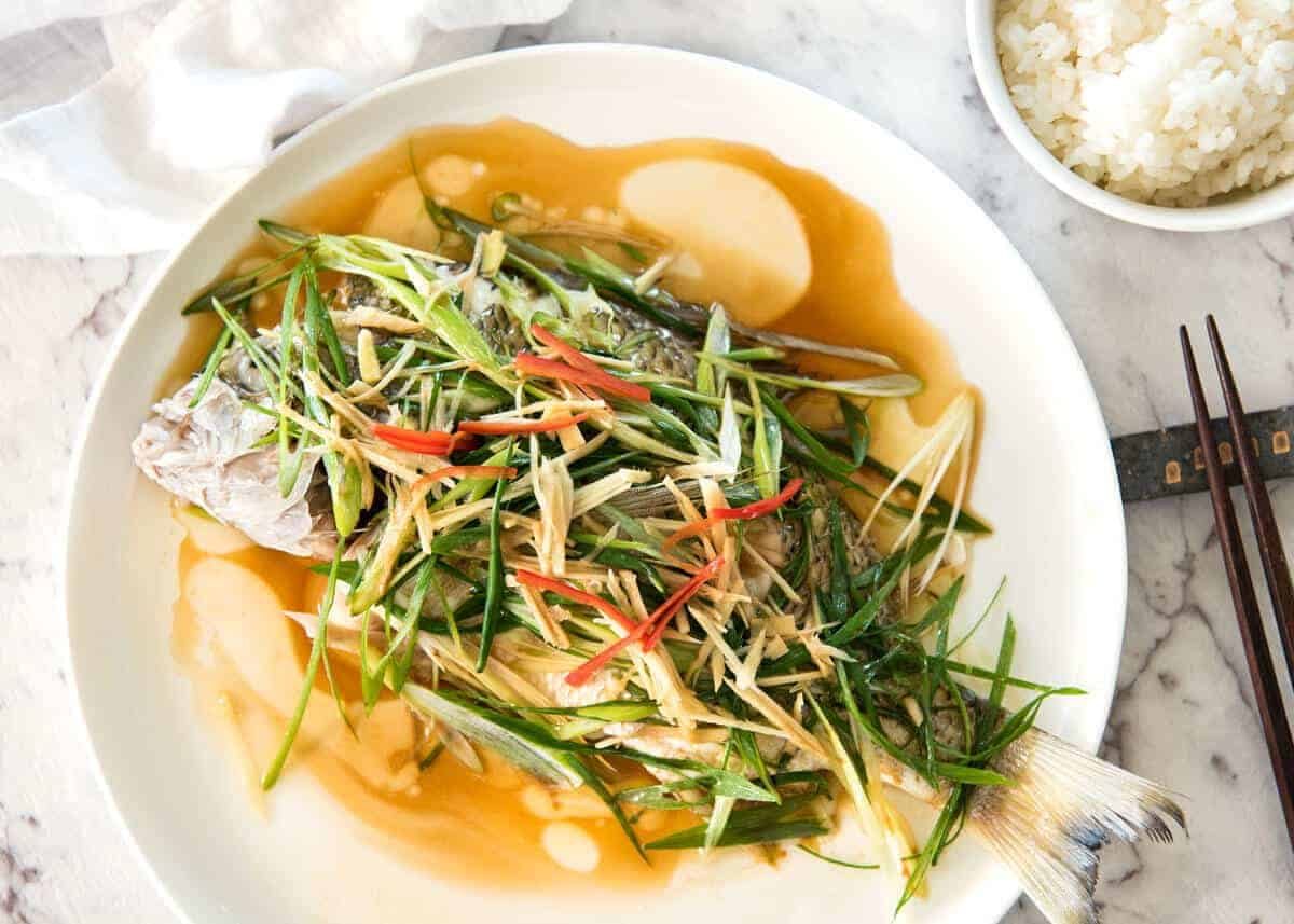 A Chinese Steamed Fish topped with Ginger and Shallots and seasonings, with hot oil poured over it to create a dramatic sizzle and an amazing sauce. So simple, yet so utterly delicious. Steam OR bake the fish! dev.recipetineats.com