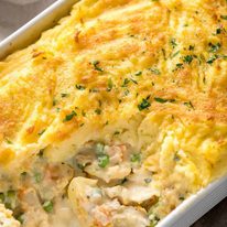 Close up of Fish Pie in white baking dish showing creamy filling with fish flakes
