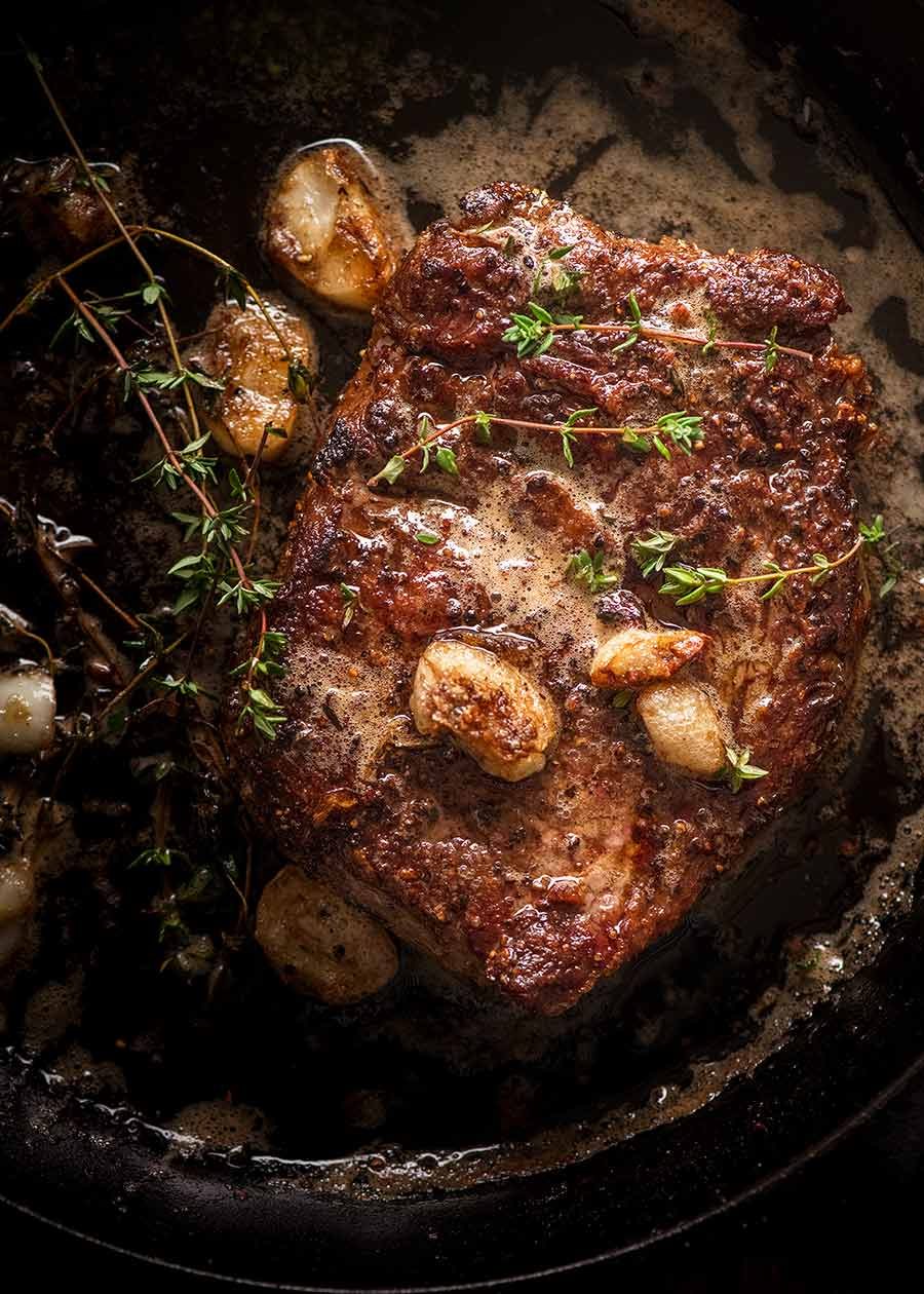 Medium rare steak in a black skillet with garlic thyme butter, fresh off the stove