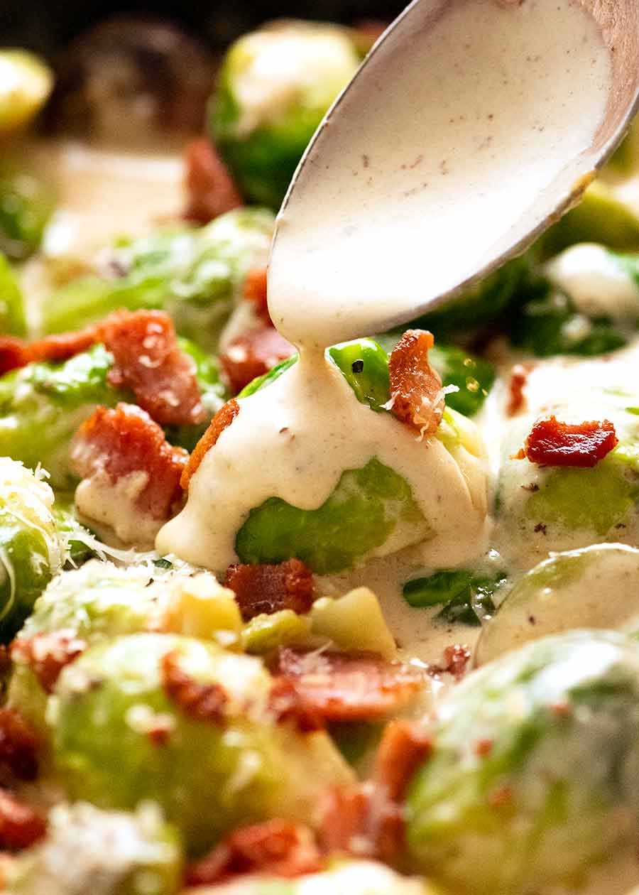 Close up of spoon drizzling creamy sauce over saut&eacute;ed brussels sprouts