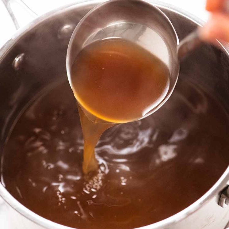 Ladle scooping up hot beef stock from pot