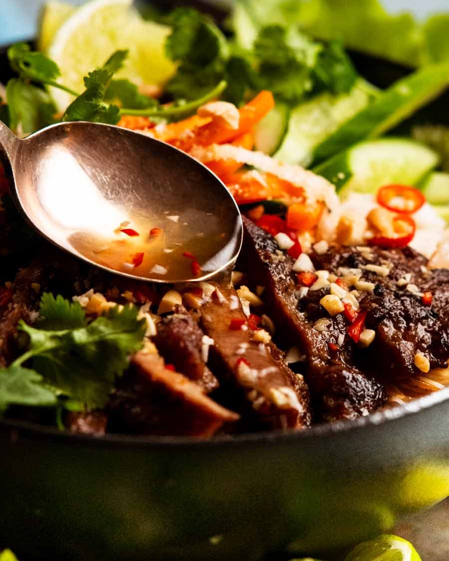 Nuoc cham sauce being spooned over Vietnamese noodles with lemongrass pork (B&uacute;n thịt nướng)